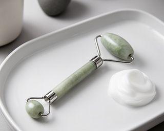 Jade-Roller liegt neben milder Reinigungslotion auf einem weissen Keramiktablett